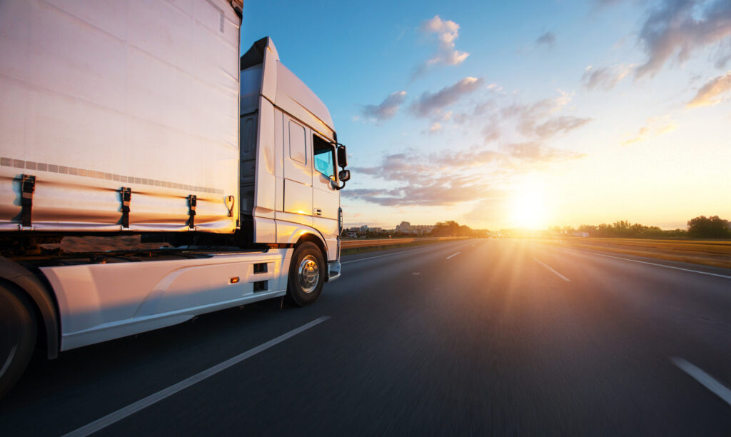 European truck driving on the asphalt road in rural landscape at sunset
